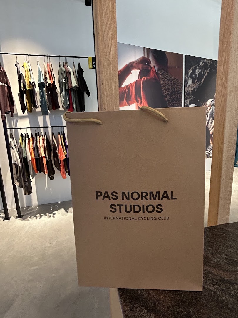 A Pas Normal Studios shopping bag in a modern retail space with clothing racks and wall art.
