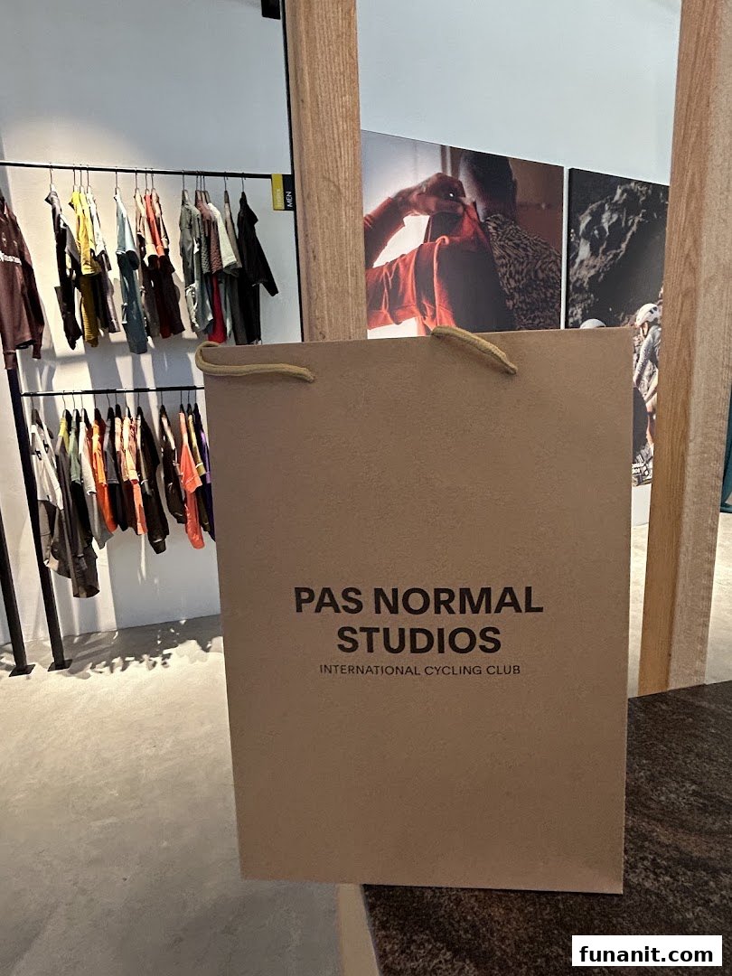 A Pas Normal Studios shopping bag in a modern retail space with clothing racks and wall art.