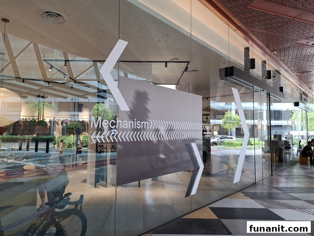 The glass facade of Pas Normal Studios Singapore, featuring 'Mechanism' branding and a view of the interior.