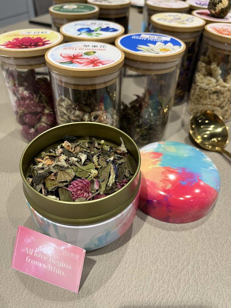 An open tin of loose leaf tea with other tea jars and a golden spoon on a table.