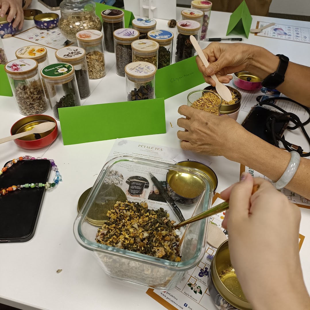 Hands blending various dried tea ingredients from jars on a white table during a workshop.