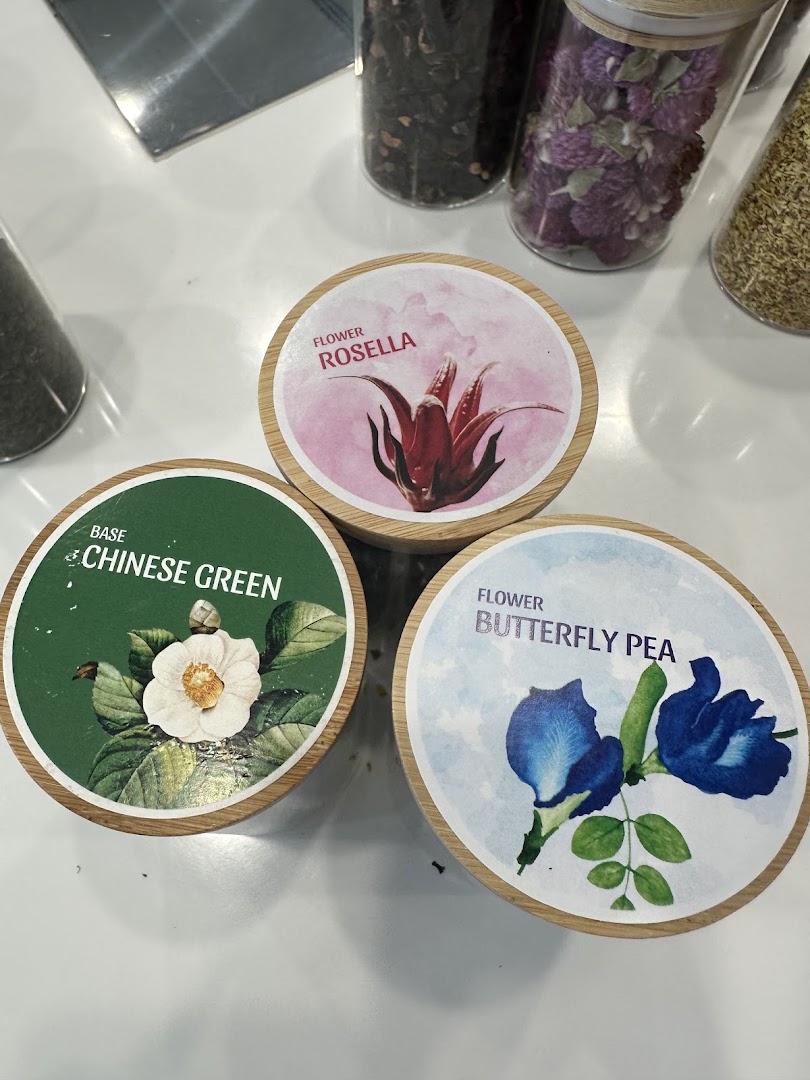 Three round containers displaying labels for Rosella, Chinese Green, and Butterfly Pea tea ingredients.