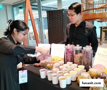 Two staff members serve tea samples from a display with various tea blends and brewing pots.