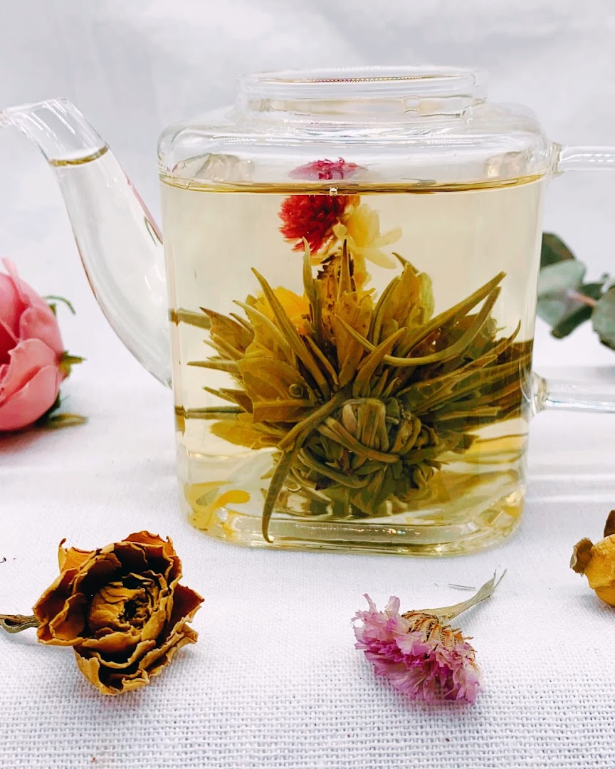 A clear glass teapot showcases a beautiful blooming tea flower unfurling in hot water.