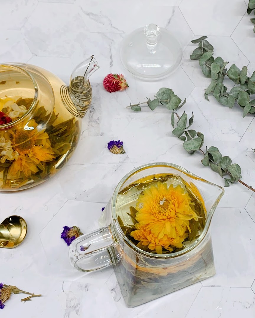 Blooming tea unfurls in elegant glass teapots, surrounded by decorative dried flowers on a marble surface.