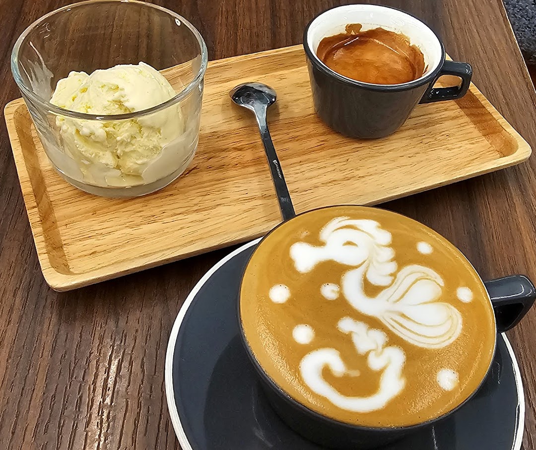 A beautifully crafted latte with seahorse art, an espresso shot, and vanilla ice cream on a wooden tray.