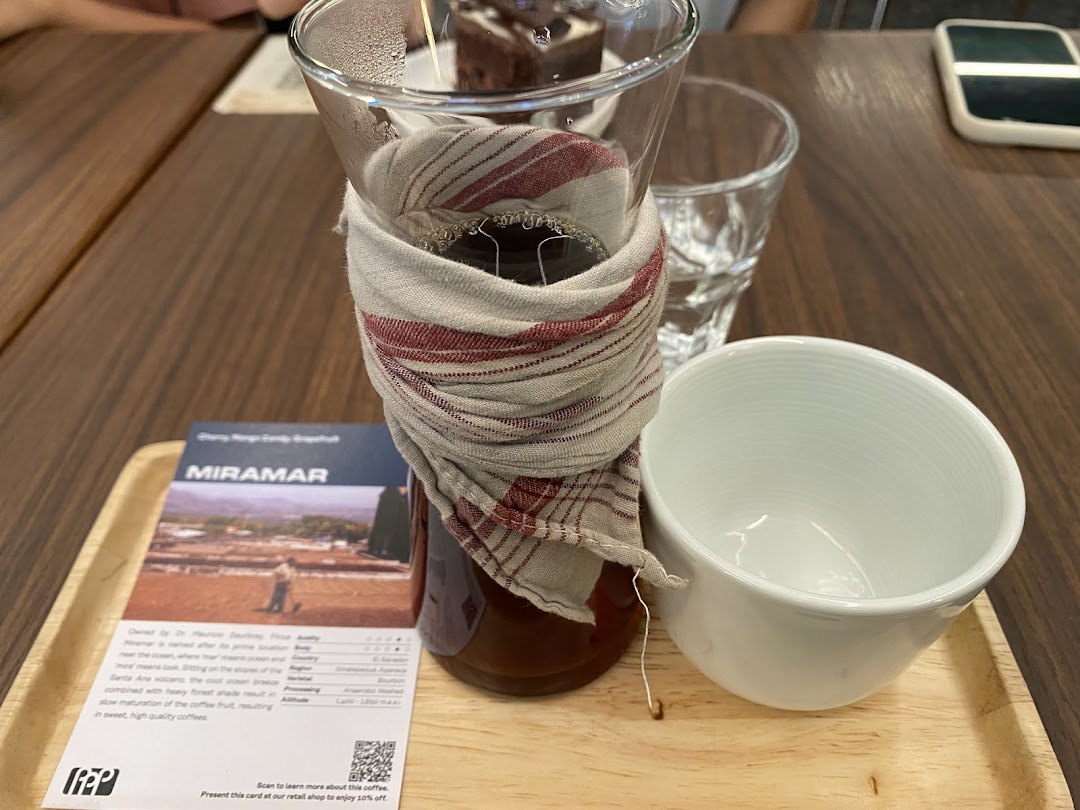 A pour-over coffee setup with a tasting card and cup on a wooden tray.