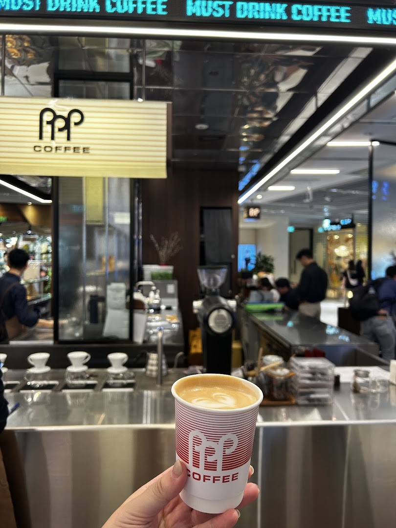 A hand holds a PPP Coffee branded cup with latte art inside the bustling coffee shop.