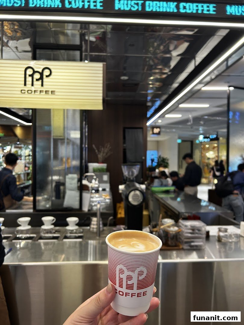 A hand holds a PPP Coffee branded cup with latte art inside the bustling coffee shop.