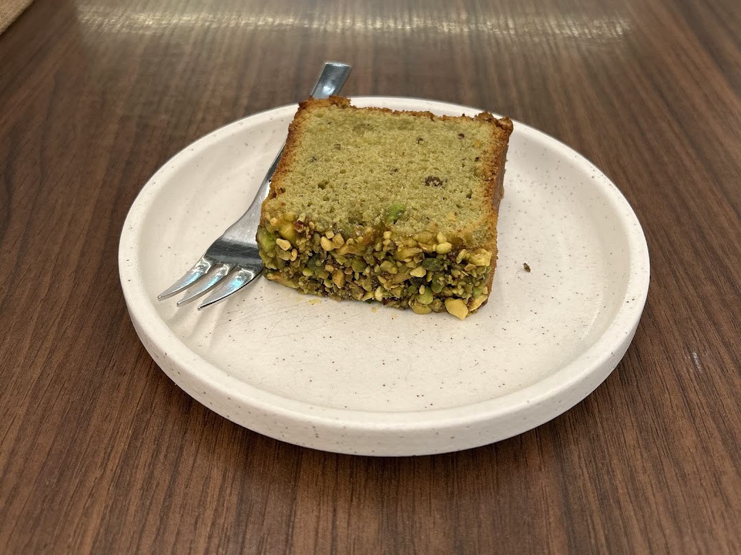 A delicious slice of pistachio cake with a fork on a white plate, ready to be enjoyed.