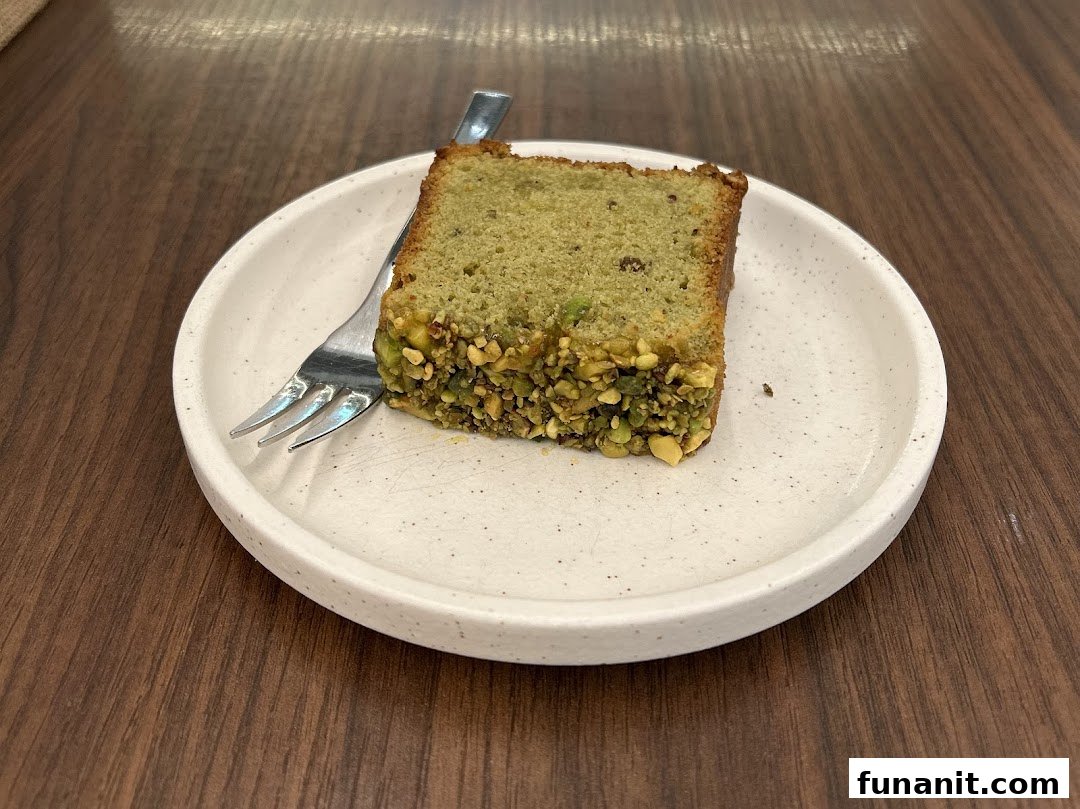 A delicious slice of pistachio cake with a fork on a white plate, ready to be enjoyed.