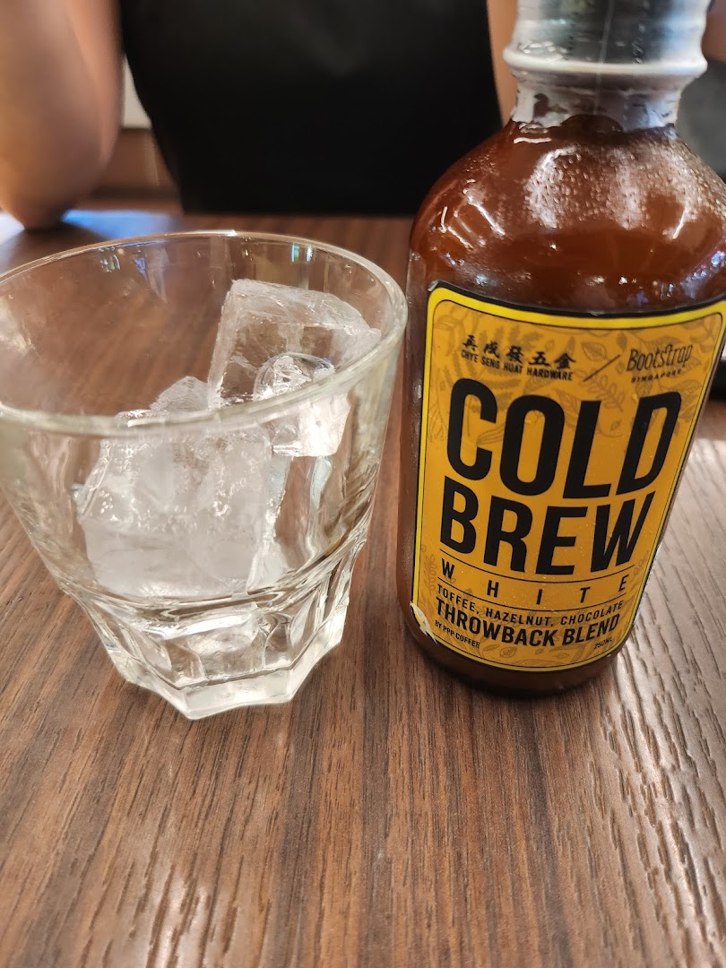 A bottle of PPP Coffee's Bootstrap Cold Brew White with a glass of ice on a wooden table.