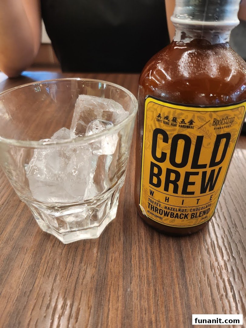 A bottle of PPP Coffee's Bootstrap Cold Brew White with a glass of ice on a wooden table.