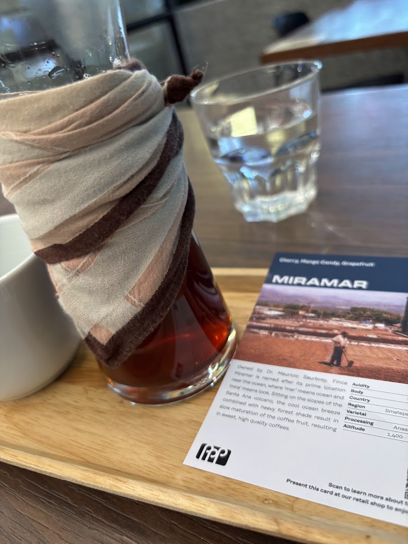 A coffee carafe, water glass, and coffee information card on a wooden tray.