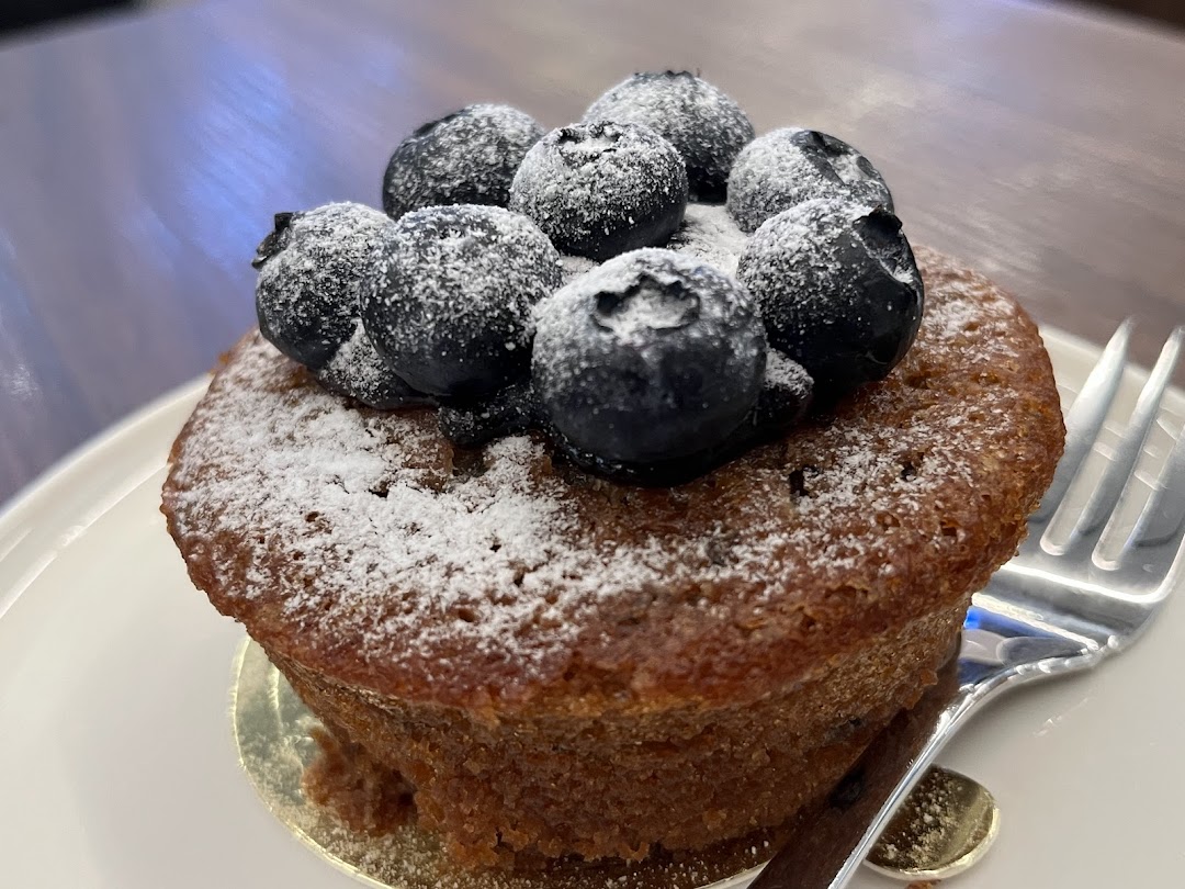 A delicious blueberry muffin or cake, dusted with powdered sugar, served on a white plate.