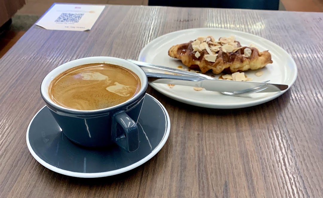 A cup of coffee and a delicious pastry with almonds on a wooden table.