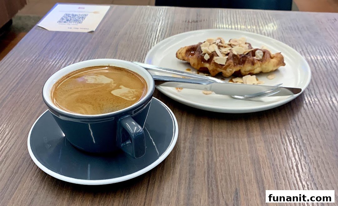 A cup of coffee and a delicious pastry with almonds on a wooden table.