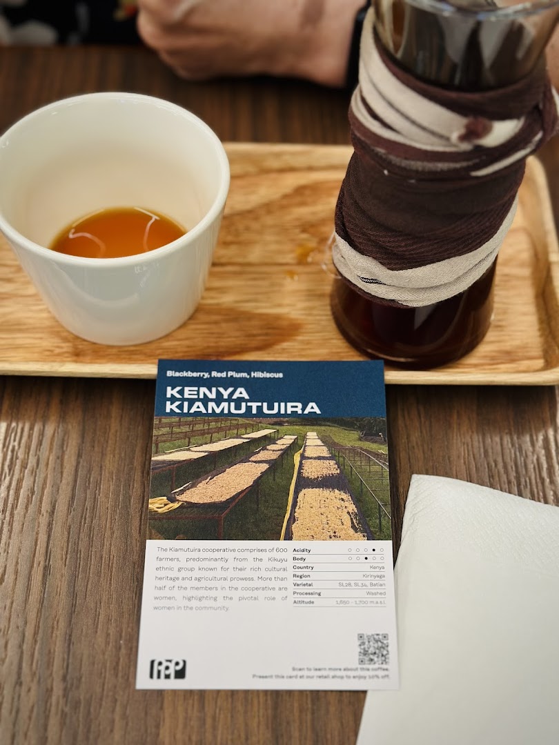 A close-up of a coffee cup, carafe, and a detailed card describing Kenya Kiamutuira coffee beans.