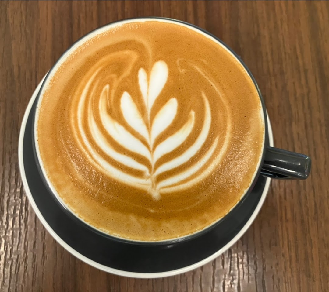 A top-down view of a latte with intricate latte art, served in a dark cup on a wooden table.