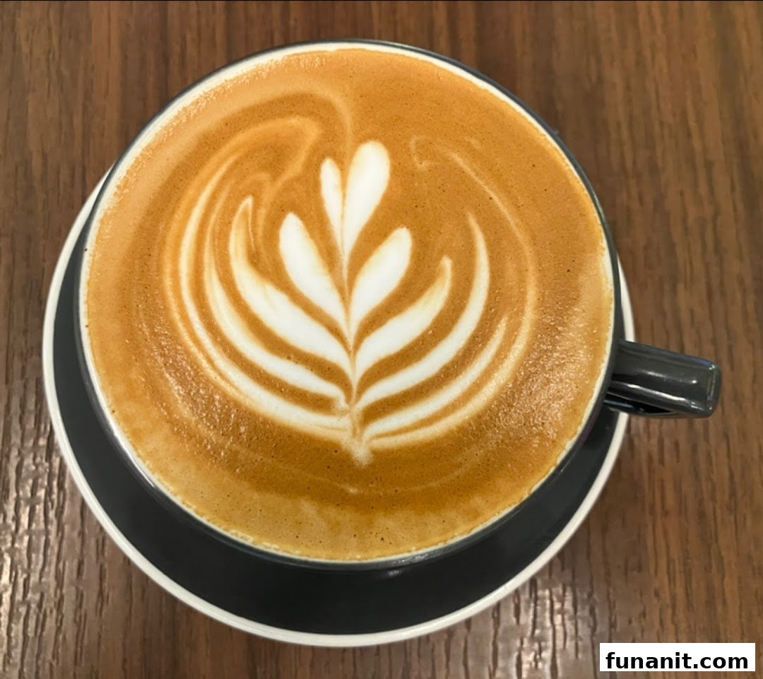 A top-down view of a latte with intricate latte art, served in a dark cup on a wooden table.