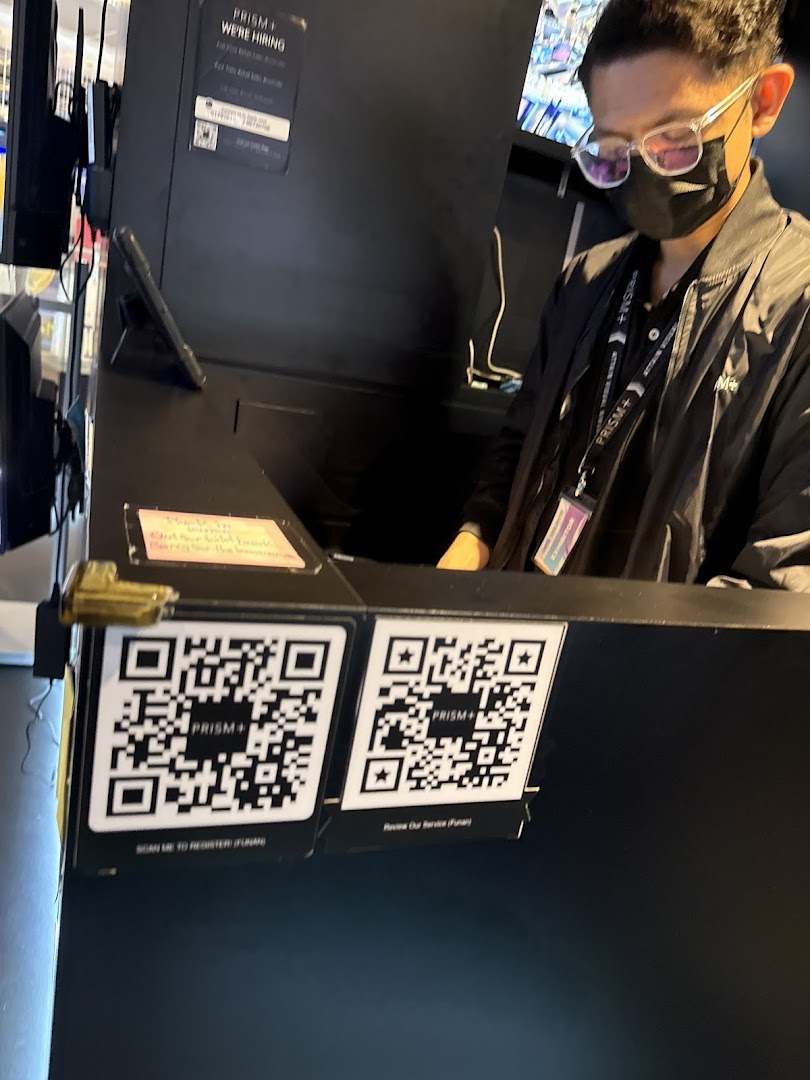 A staff member at the PRISM Funan counter, with QR codes for registration and service review.