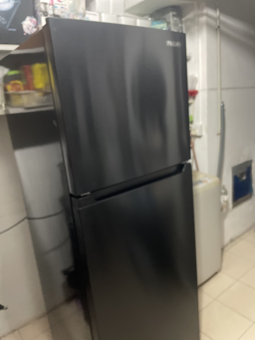 A black two-door refrigerator is seen in a utility or storage area, likely showcasing a product from PRISM.