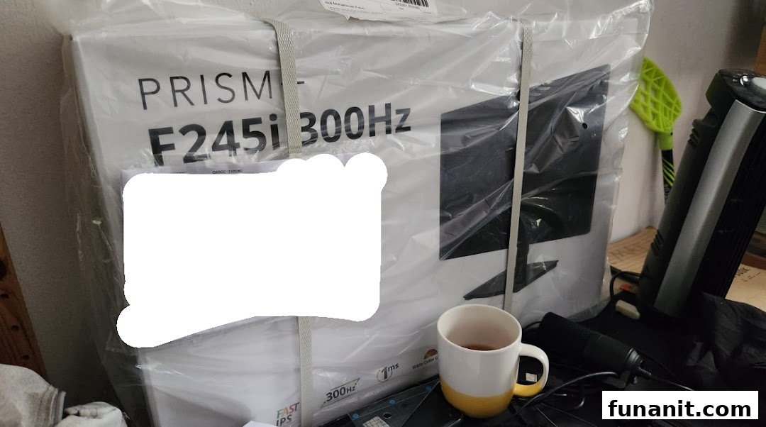 A large monitor box from PRISM Funan, still in its plastic packaging, with a mug nearby.