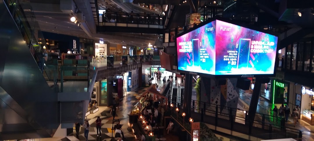 An overhead view of a modern, multi-level shopping mall interior with escalators, various shops, and people.