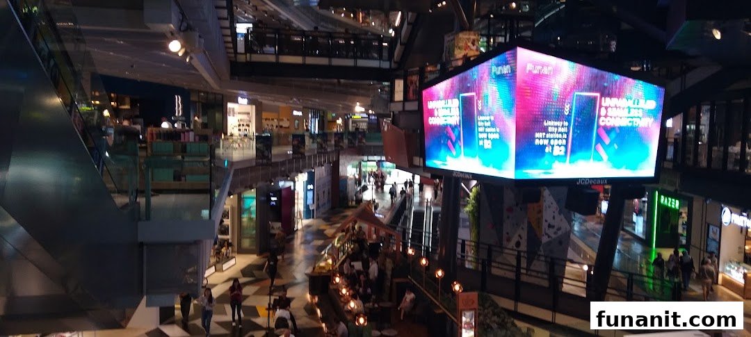 An overhead view of a modern, multi-level shopping mall interior with escalators, various shops, and people.
