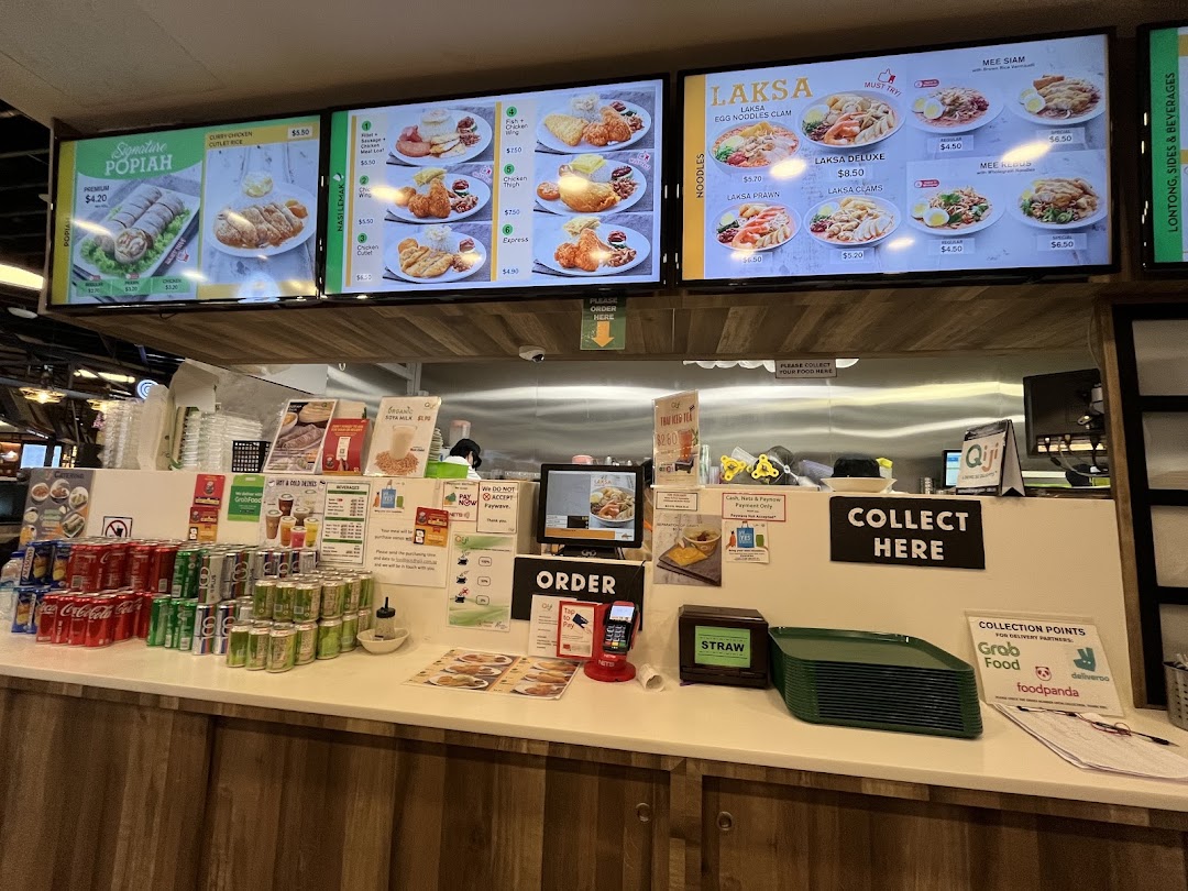A bustling food stall counter at Qi Ji, featuring digital menu boards displaying various local dishes.
