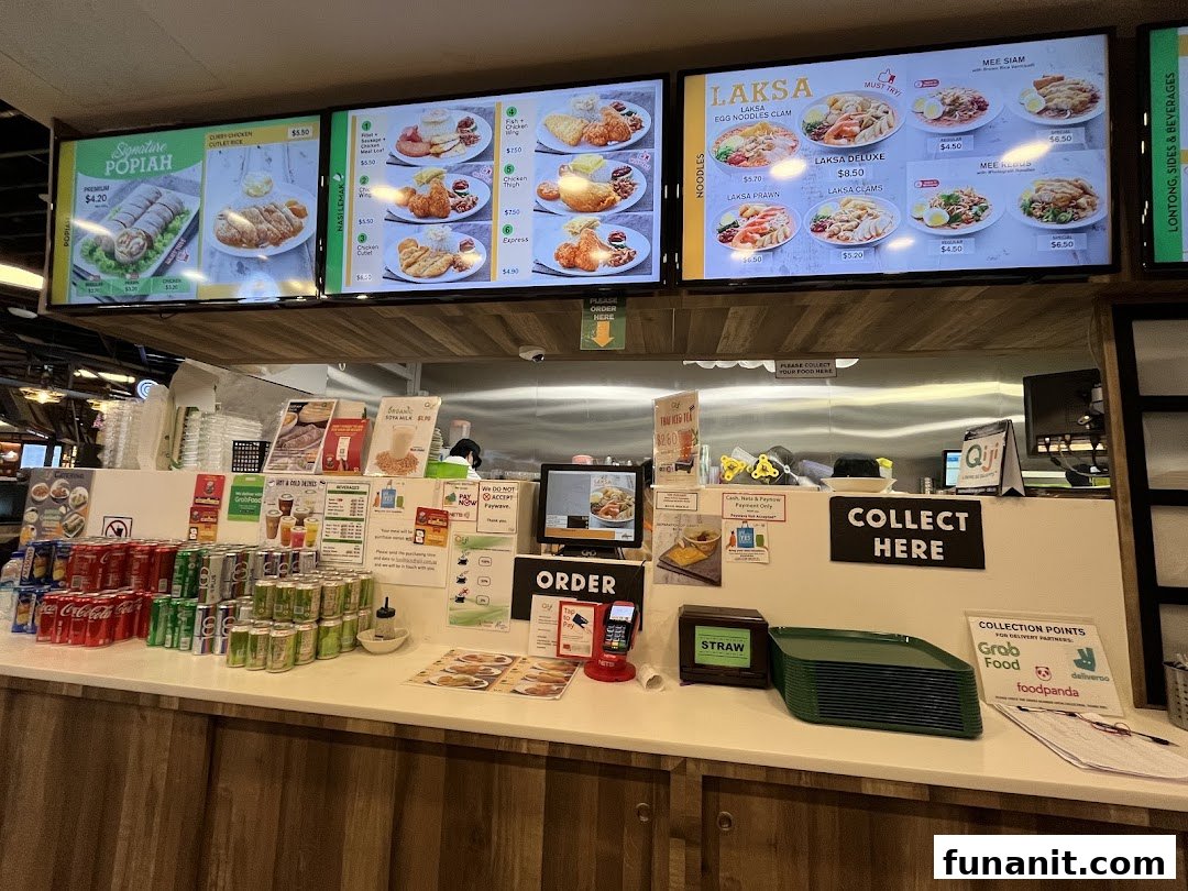 A bustling food stall counter at Qi Ji, featuring digital menu boards displaying various local dishes.