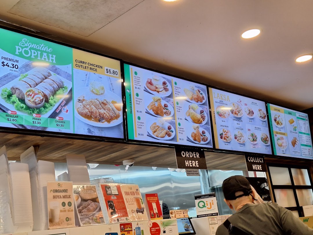 Digital menu boards display various Singaporean/Malaysian dishes and drinks at Qi Ji, with a customer at the counter.
