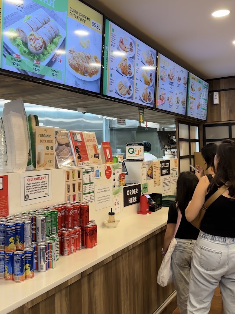 The counter of Qi Ji with digital menus, canned drinks, and customers queuing to order.