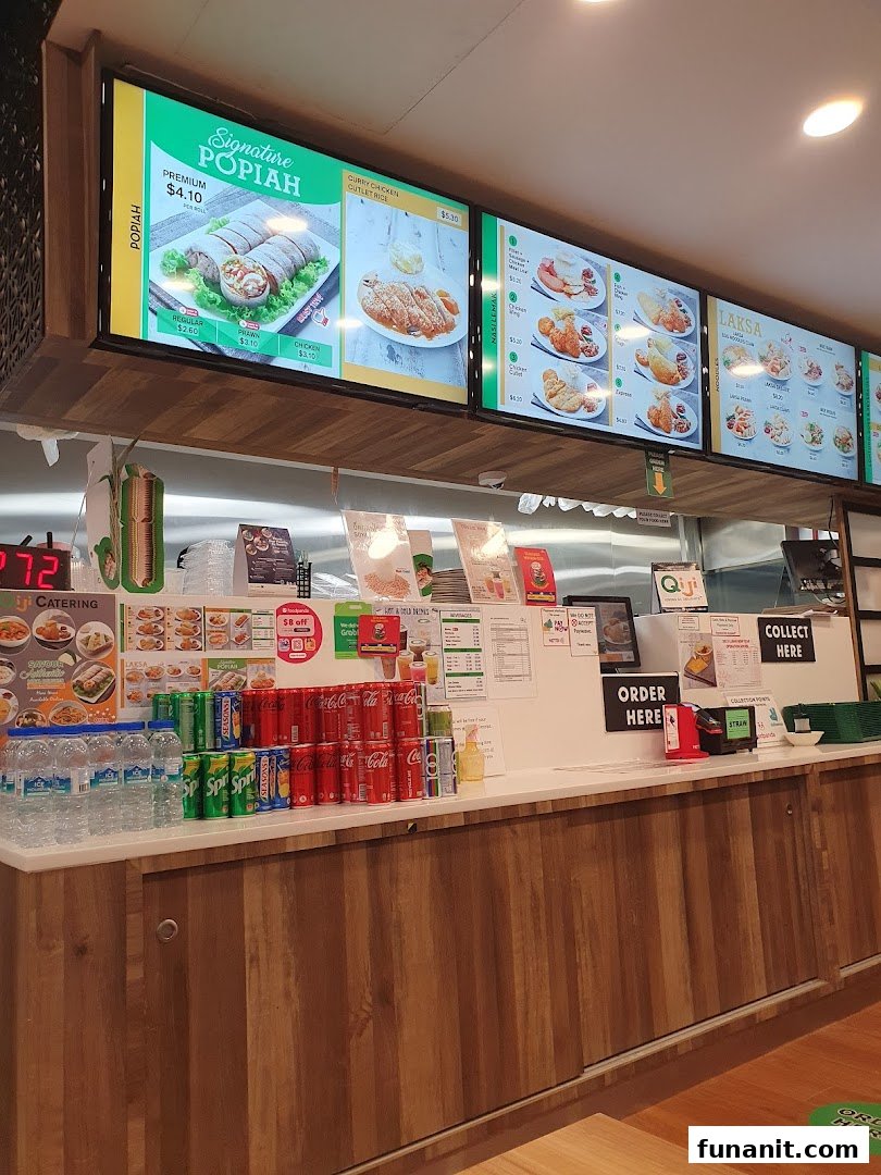 View of Qi Ji's food stall counter with digital menu boards showcasing Popiah, Laksa, and other local dishes.
