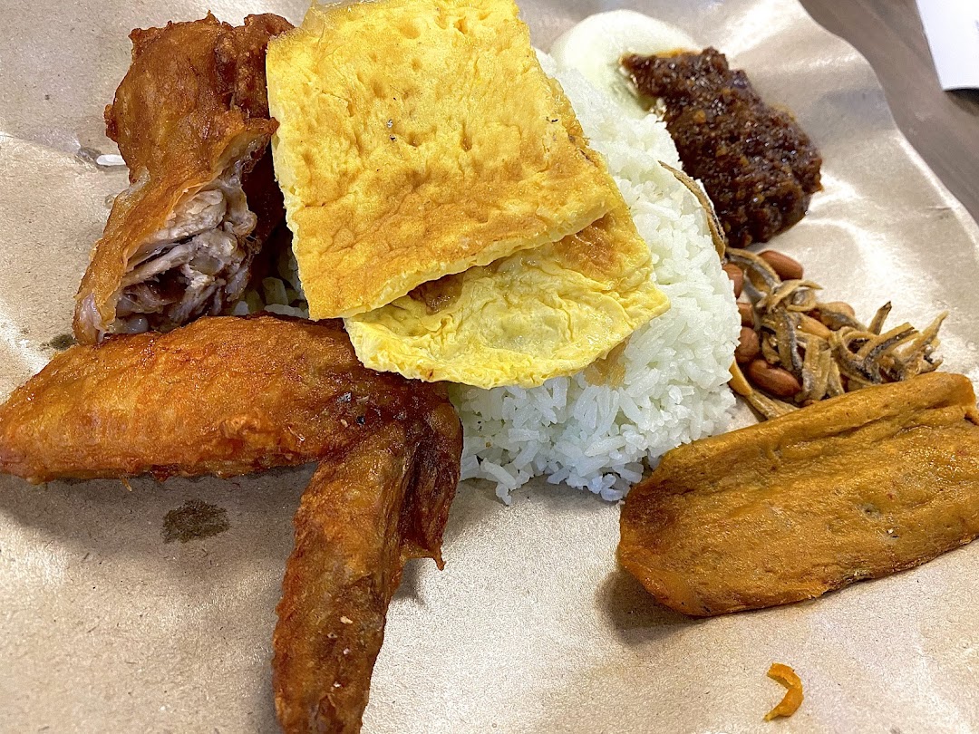 A close-up of a delicious Nasi Lemak set featuring fried chicken, fluffy rice, egg, sambal, anchovies, and peanuts.