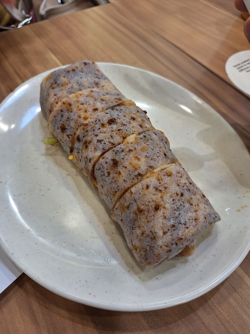 A close-up shot of a freshly prepared, sliced popiah (spring roll) served on a white plate.