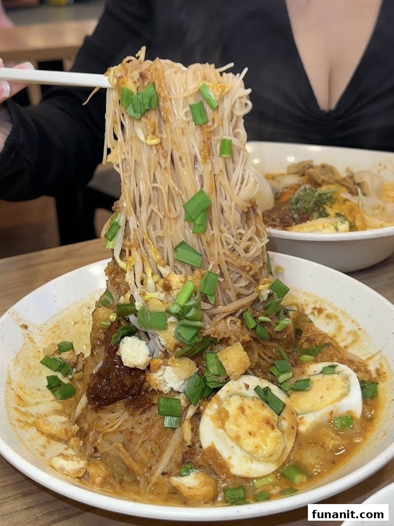 A close-up of a person lifting flavorful noodles from a rich, saucy dish with eggs and sprouts.