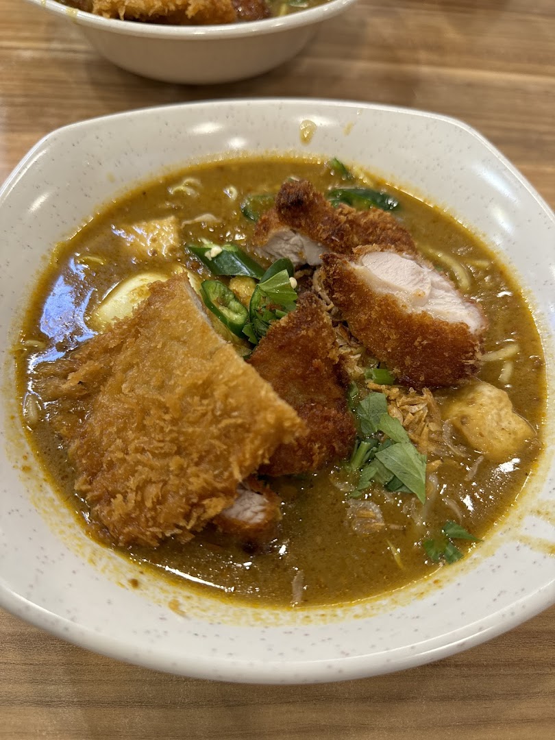 A close-up of a delicious bowl of curry noodles topped with crispy fried chicken cutlets and fresh herbs.