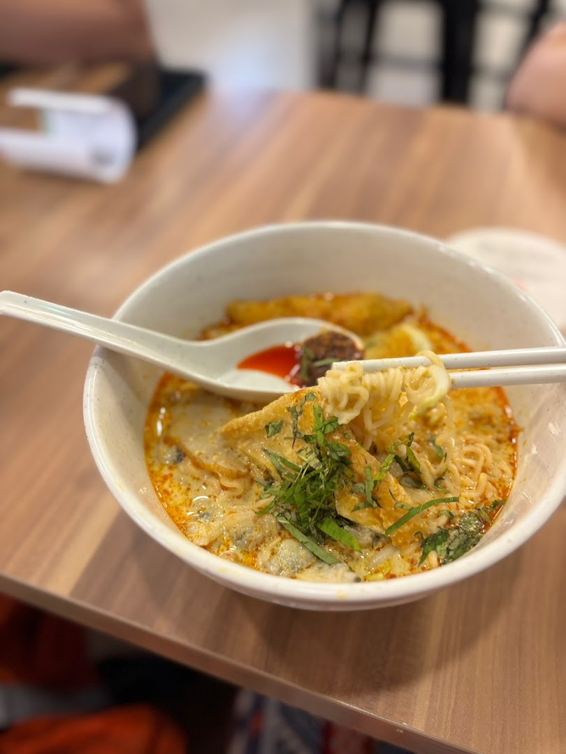 A close-up of a delicious bowl of noodles with rich broth, garnished with herbs and various toppings.