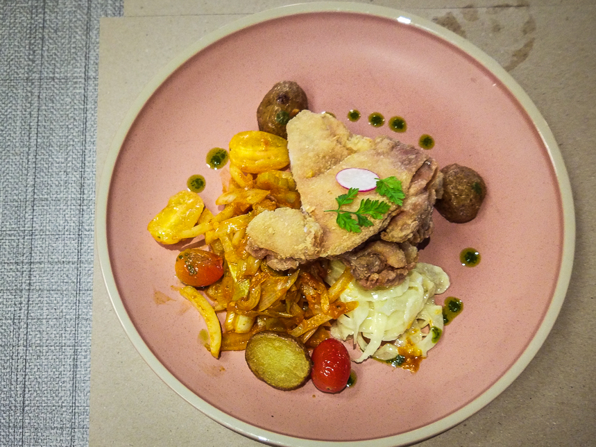 A beautifully plated dish featuring crispy fried chicken, sautéed vegetables, and fresh garnishes on a pink plate.
