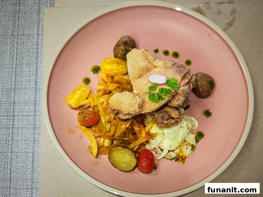 A beautifully plated dish featuring crispy fried chicken, sautéed vegetables, and fresh garnishes on a pink plate.