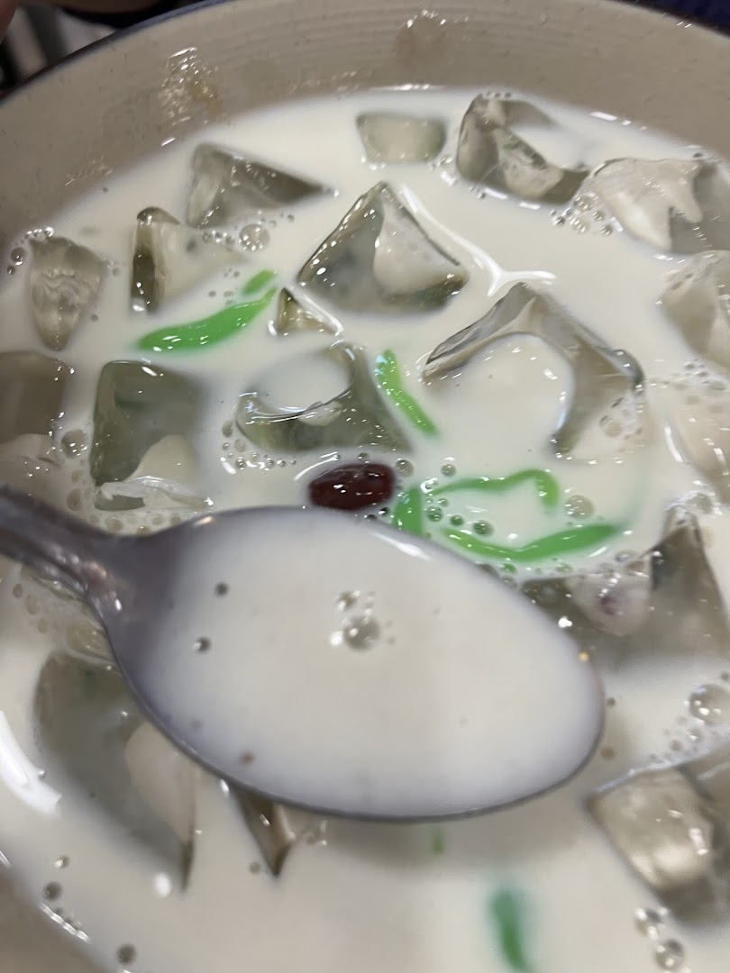 A close-up of a refreshing bowl of cendol with ice, green jelly, and red beans.