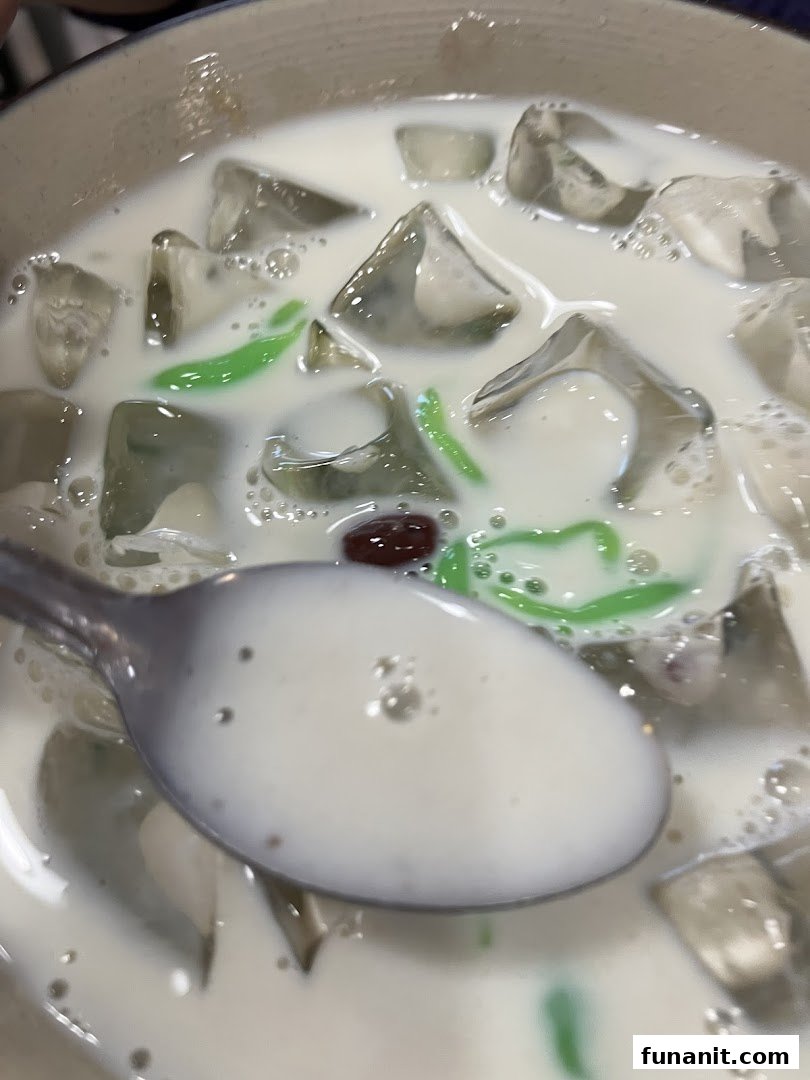A close-up of a refreshing bowl of cendol with ice, green jelly, and red beans.