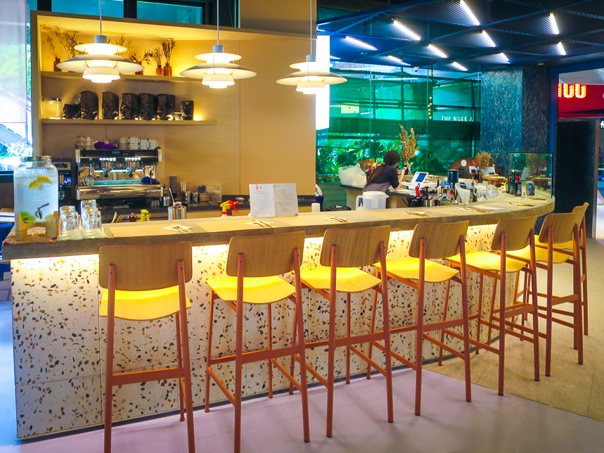 A modern coffee bar with a long counter, bar stools, and a barista station.