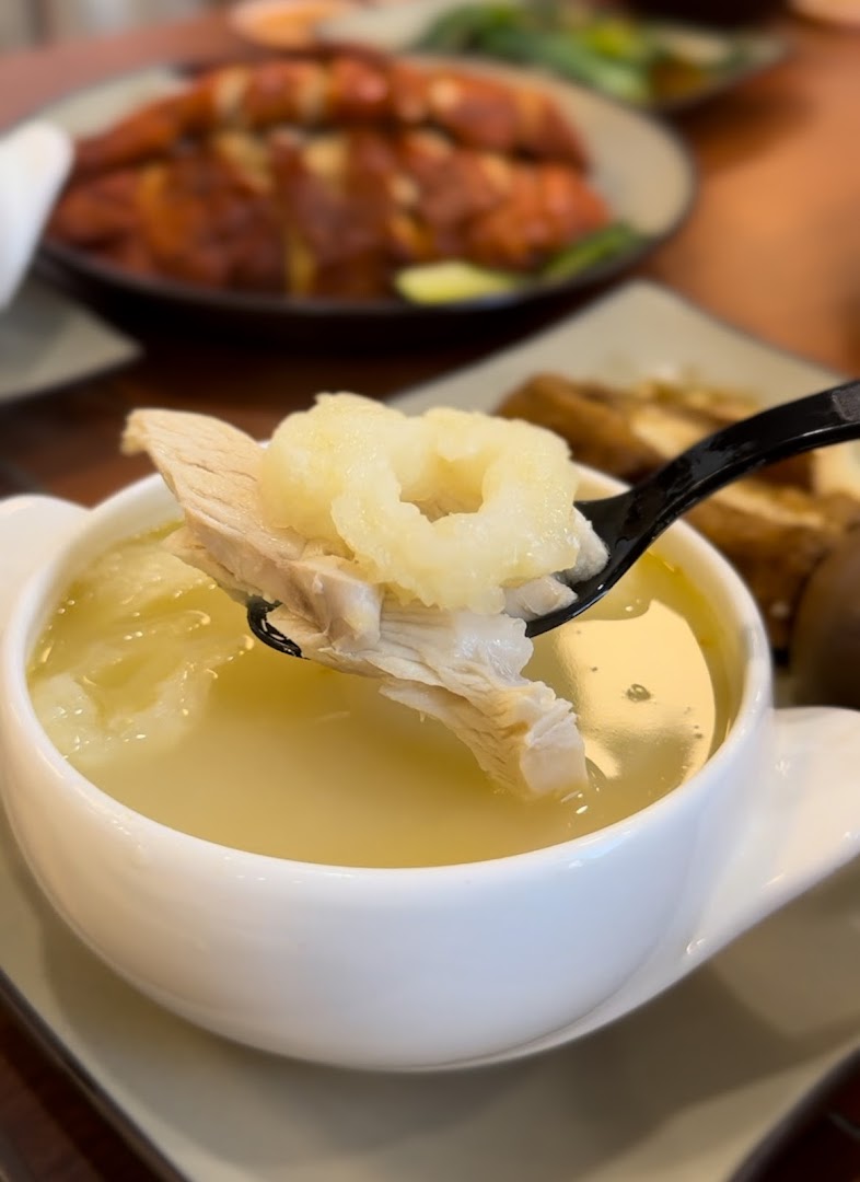 A spoon lifts tender chicken and a unique ingredient from a bowl of clear soup.