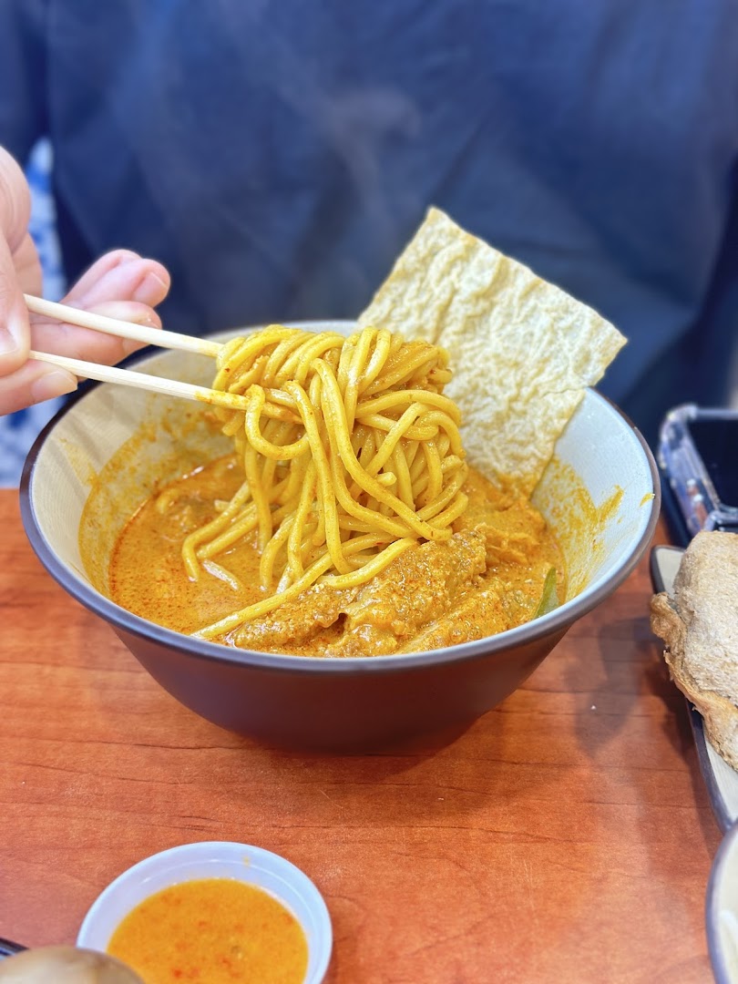 A close-up of a person enjoying a vibrant bowl of curry noodles with chopsticks at Raffles Coffee and Toast.
