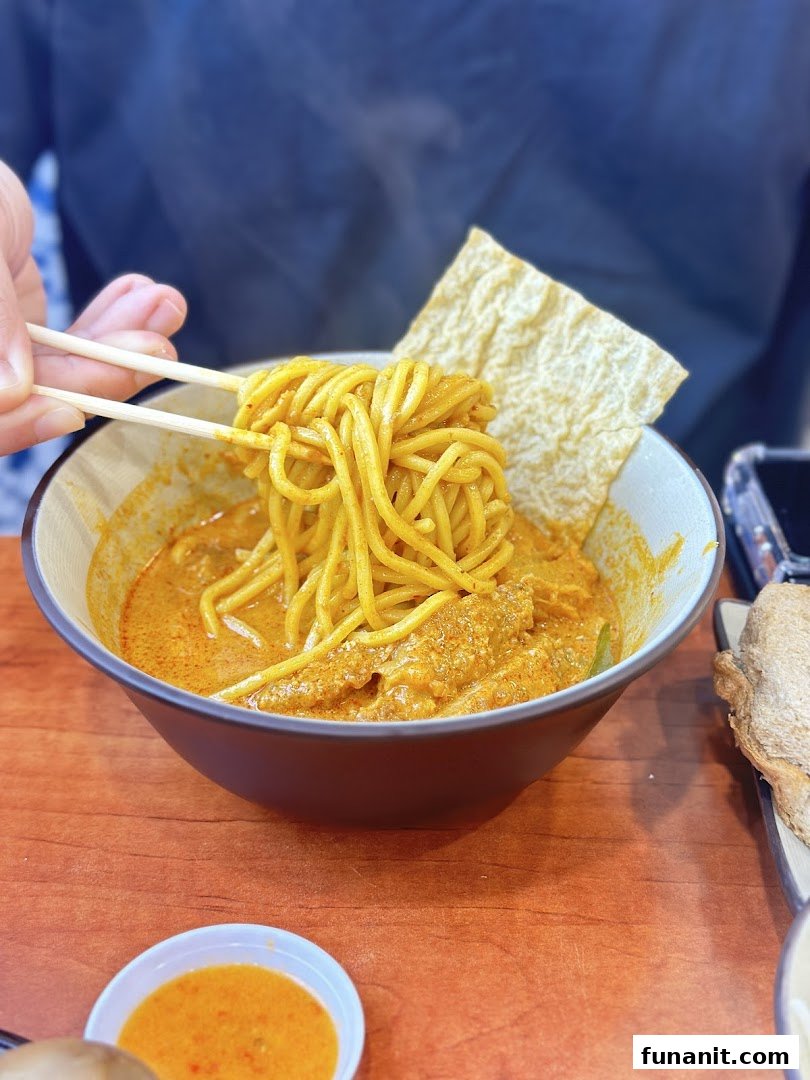 A close-up of a person enjoying a vibrant bowl of curry noodles with chopsticks at Raffles Coffee and Toast.