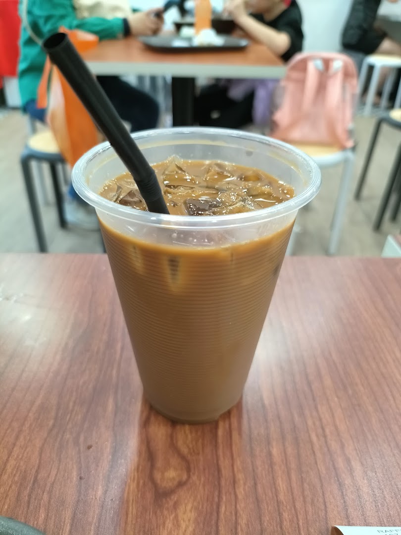 A refreshing iced coffee with a straw on a wooden table inside Raffles Coffee and Toast.