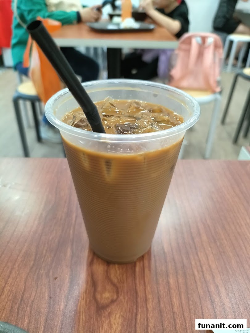 A refreshing iced coffee with a straw on a wooden table inside Raffles Coffee and Toast.