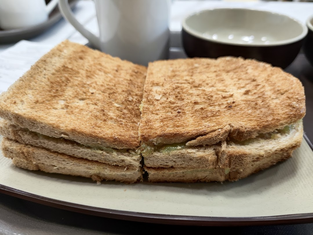 A close-up of golden-brown kaya toast served on a plate with a beverage in the background.